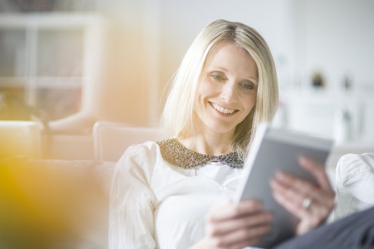Portrait of smiling blond woman using mini tablet at home