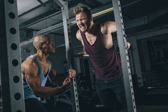 Two friends exercising dips at power rack in gym