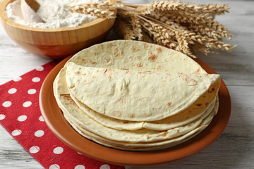Stack of homemade whole wheat flour tortilla on plate, on wooden table background