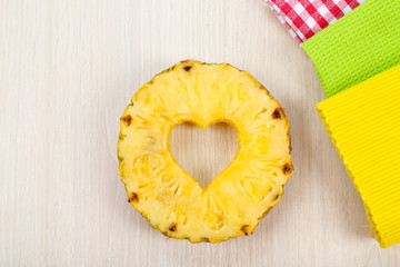 Pineapple slice with cut in shape of heart with napkins on wooden background