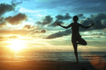 Fototapeta premium Silhouette of woman standing at yoga pose on the beach during an amazing sunset. Meditation, balance, harmony and tranquility concept.