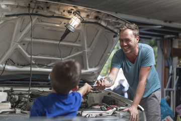 Son helping father in home garage working on car