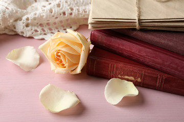 Fresh rose flower with old book and letters on color wooden table background. Vintage concept