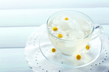 Glass of cold chamomile tea with ice cubes and chamomile flowers on color wooden background
