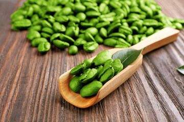 Coffee beans with leaf in spoon on wooden table close up