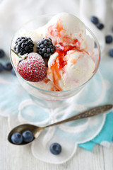 Delicious ice cream with fresh frozen berries and sauce, on color wooden background