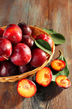Ripe plums in bowl on wooden background