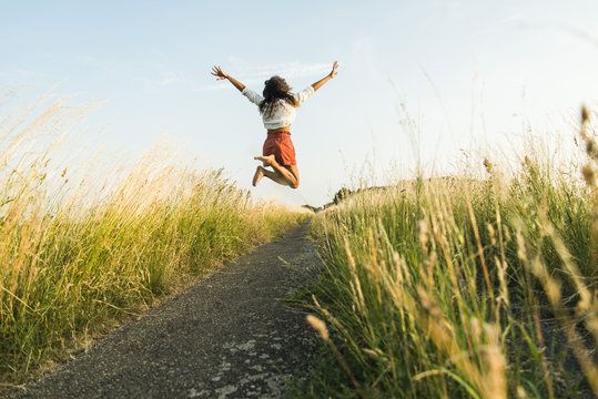 Enthusiastic young woman jumping on path in field