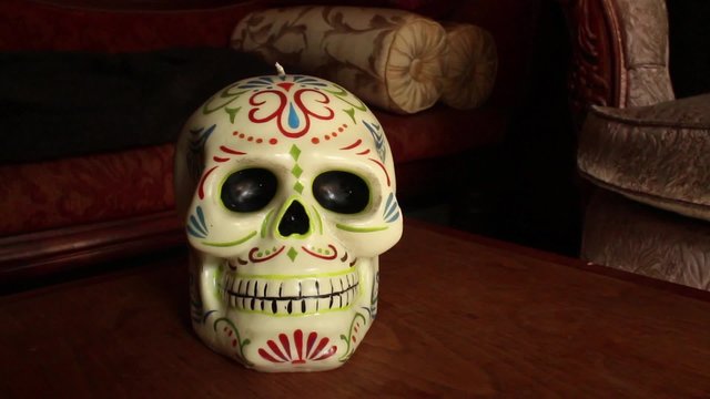 Wider shot of colorful Mexican skull, dolly out and hold; reveal light pattern on table with vintage couch behind