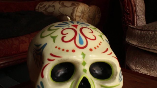 Dolly out from ECU Mexican wax skull, hold at medium close up; continue dolly out to wider shot
