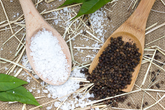 Sea salt and black pepper in wooden spoon on burlap sack background