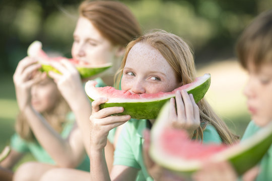 Portrait of girl eating slice of watermelon watching boy