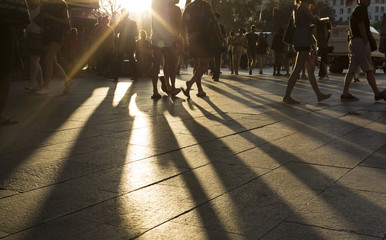 Crowds walking in a busy district as the sun flares between them in the late afternoon - 89598720
