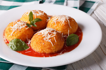 Delicious fried arancini rice balls in tomato sauce close-up. horizontal
