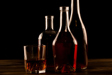 glass of whiskey with ice and a bottle on a wooden table. Cognac, brandy.