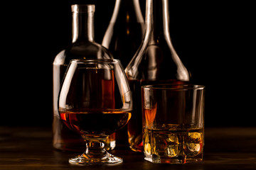 glass of whiskey with ice and a bottle on a wooden table. Cognac, brandy.
