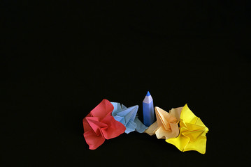 Яркие краски в виде оригами цветов (розовых, голубых, желтых) и карандаша на черном фоне