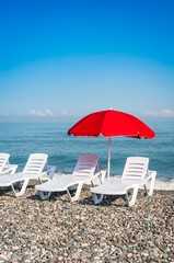 Beach chairs and red umbrella on shingle beach
