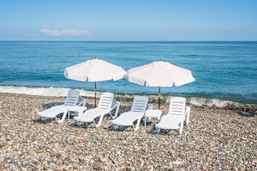 Four white plastic beach chairs and two white parasols on the be