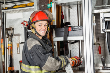 Obraz premium Happy Firefighter Fixing Water Hose In Truck