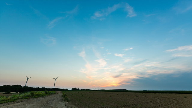 Time lapse sequence of rotating wind turbines during a sunset with a dirt road leading into the image.