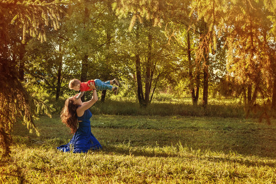 Young Mother Playing with her Baby Son Outdoor in Green Forest Park
