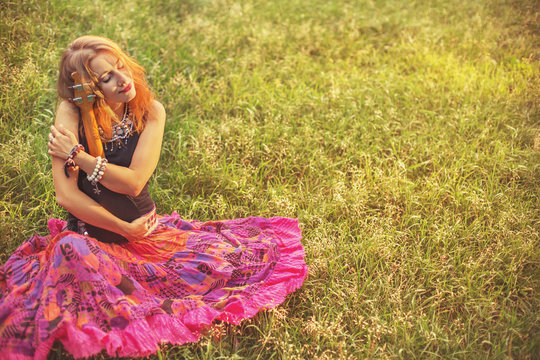 Young Happy Woman Enjoy on Green Grass in the Field with Wild Flowers Background, holds Small Guitar Ukulele