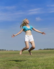 The happy woman jumps in a summer green field against the blue sky...