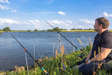 M&auml;nnlicher Angler sitzt am Fluss bei blauem Himmel