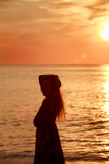 Fototapeta premium slim girl in long dress against sunrise over sea
