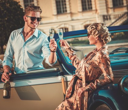 Wealthy couple with champagne near classic convertible