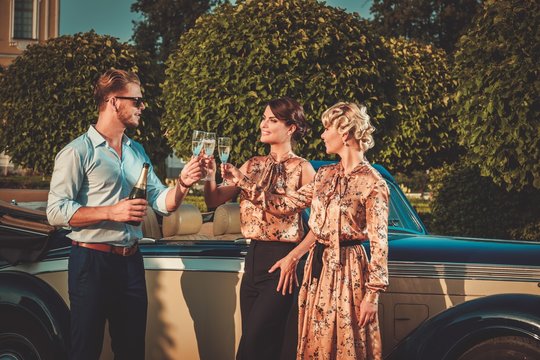 Wealthy friends drinking champagne near classic convertible