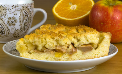 The composition of a piece of apple pie on a plate, an apple and orange halves.