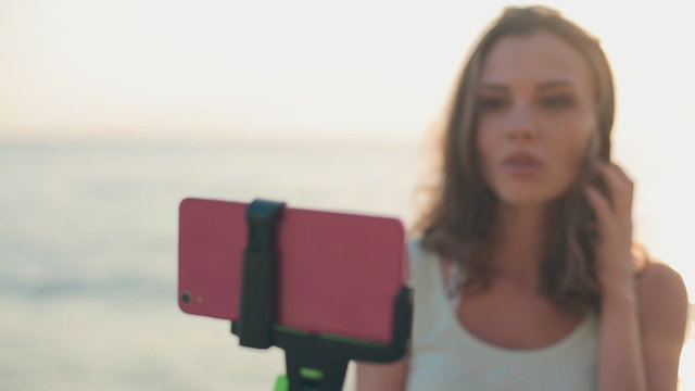 Attractive girl standing in the sea with a monopod and makes