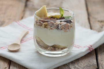 Yogurt with muesli and banana in small glass.