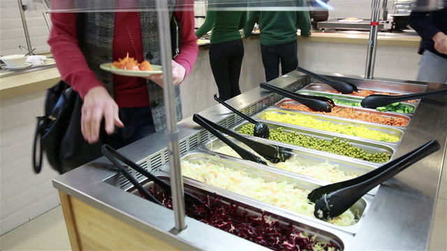 A woman taking vegetables in the salad bar. Lunch in the canteen.