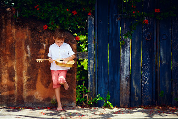 cute young boy playing guitar near the summer old fence