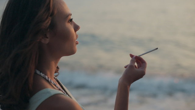 Girl smoking a cigarette at sunset near the sea