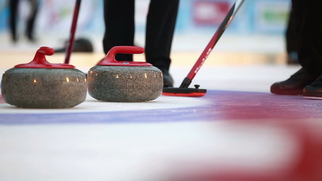 Players curling throw stones on the ice.