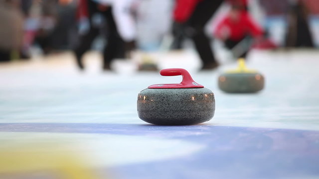 Players curling throw stones on the ice.