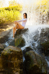 Beautiful girl sits on a rock near the waterfall.