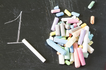 One piece of chalk against the pile of crayons of different colors on a black background blackboard opposition, number one. one in a thousand