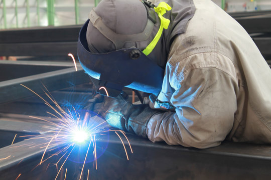 welder is welding steel structure with safety mask and safety gloves in factory
