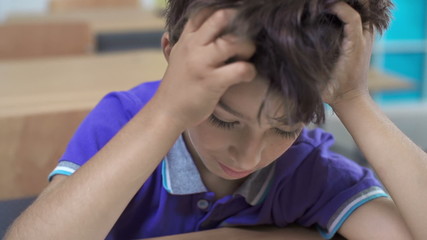 Thoughtful schoolboy scratching his head and chin during exam 