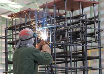 welder is welding steel frame in factory with safety equipment