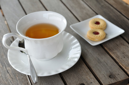 English tea in white cup with cookie on wooden table.