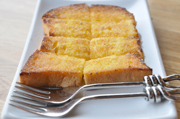 Toast with butter and sugar in white plate with double fork on w