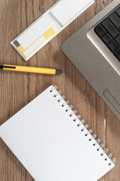 Blank notepad and laptop on office wooden table, top view