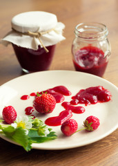 Homemade strawberry jam (marmelade) in jars on wooden background.