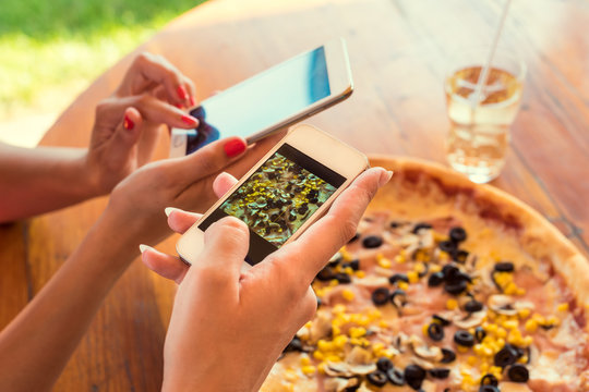 Female friends using smartphones to take photos of their pizza